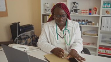 Klinikte çalışan bir kadın, iş yerinde tıbbi ekipman ve dosyalarla stres altında bardakları çıkarıyor..