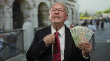 Takım elbiseli son sınıf öğrencisi elinde Czech Koruna banknotları Roma Kolezyum Caddesi 'nin yakınındaki açık havada el kol hareketleri yapıyor..