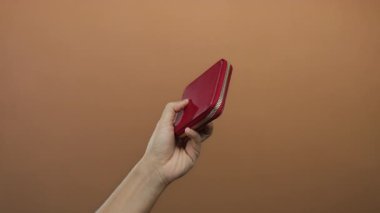 Kahverengi arka planda kırmızı cüzdanı olan beyaz bir adam, izole edilmiş basitlik ve modern zarafeti minimalist tarzda sergiliyor..