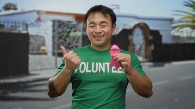 Pembe kurdeleli ve gönüllü tişörtlü genç adam, şehir sokaklarında meme kanseri farkındalığını destekliyor.