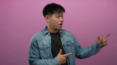 İzole edilmiş pembe arka planda ifade ile parlayan genç bir adam kot ceket giyiyor, oyunculuk ve enerji gösteriyor.