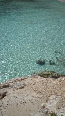 Berrak turkuaz su, Mallorca 'da güneşli bir sahilde kayalık kıyılara nazikçe döner. Doğanın dingin güzelliğini ve rahatlamasını gözler önüne serer..
