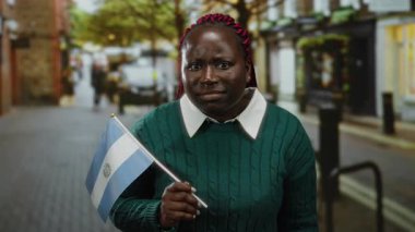 Şehir caddesinde kendine güveni tam bir Salvador bayrağı taşıyan kadın, farklı kimlikler ve açık hava ortamında uluslararası kültür karışımı sergiliyor..