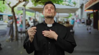 Rahip şehir terasında karşıdan karşıya geçerken arka planda insanlar şehir ortamında inanç ve sadakat gösteriyorlar..