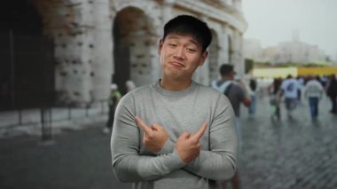 Arka planda bulanık bir sokak sahnesiyle tarihi Roma Stadyumu 'nun dışında güvenle poz veren genç Çinli bir adam..