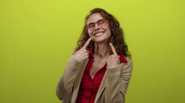 Gülüşünü işaret eden bir kadın, parlak sarı bir arka planda gözlükleriyle neşe ve güven saçıyor..