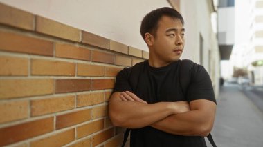 Kentin tuğla duvarına karşı duran genç adam gündelik şehir ortamını ve kendine güveni sergiliyor..
