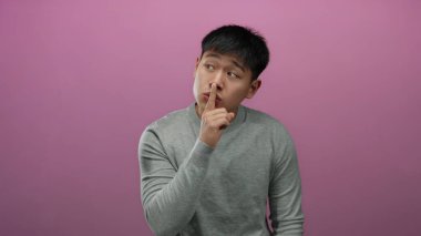 Pembe arka planda dudakları üstünde sessizlik için el kol hareketi yapan genç adam gizemli ve sakin bir ortam izlenimi uyandırıyor..