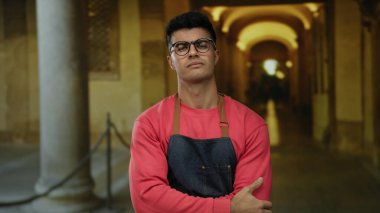 Önlüklü genç adam, tarihi üniversite koridorunda özenle poz veriyor. Mimarinin zarafetini ve geleneksel akademik ortamların çekiciliğini sergiliyor..