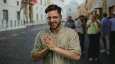 Gündüz vakti şehir sokaklarında kaldırım taşı yolda gülümseyen sakallı genç bir adam canlı bir şehir manzarası yakalıyor.