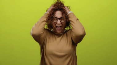 Sarı arka planda hayal kırıklığına uğramış, orta yaşlı, kıvırcık esmer saçlı, rahat süveter ve gözlük giyen, elleri umutsuzluk içinde olan bir kadın..