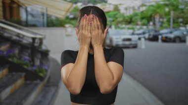 Siyah mahsul bluzu giyen genç sarışın kadın, park yeri kaldırımında el hareketini durdurmak için avuçlarını kaldırıyor..