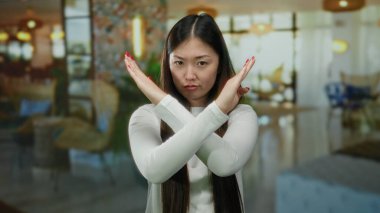 Şık bir otel ortamında kollarını kavuşturup el kol hareketi yapan bir kadın net bir ifade ve canlı bir ortam sergiliyor..