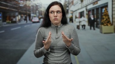 Kadın kışın şehir caddesinde, bulanık yayalar ve şehir dekorasyonlarıyla çevrili, şaşkın bir ifadeyle kendini işaret ediyor..