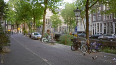 Amsterdam 'ın kanalları boyunca park halindeki bisikletlerin, lambaların ve klasik Hollanda mimarisinin yer aldığı manzaradan arındırılmış bir cadde. Yay yaprakları yeşil bir şehir yaratıyor..