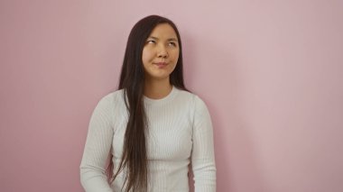 Pembe arka planda izole edilmiş genç Çinli kadın çekici ve güzel görünüyor. Uzun saçlı ve zarif gülüşü var. Duvarın karşısında duruyor..