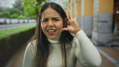 Yeşillik ve şehir zeminiyle dikkatlice dinleyen bir kadın, şehir ortamında merak ve bağlılık gösteriyor..