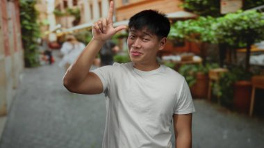 Genç adam neşeli bir jest yapıyor canlı bir şehir caddesinde, yeşil gömlekli, beyaz gömlekli, şehir dışı enerjisini ve gündelik havasını yakalıyor..