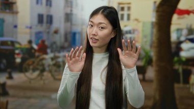 Bulanık arka planda sakin bir şekilde el kol hareketi yapan kadın, sakin ve barışçıl bir ifadeyi vurgulayan Asyalı bir şehir ortamına işaret ediyor..