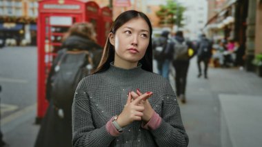 Dışarıda, kırmızı telefon kulübesinde, gri süveter giyen bir kadın. Düşünceli bir ifade..