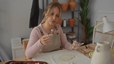 Kadın seramik stüdyosundaki ahşap masanın üzerinde metal şekillendirme aletini tutuyor. Yaratıcılığın farkındalığına odaklanıyor..