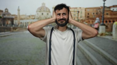 Eski Roma 'da sakallı, sıkıntılı görünen İspanyol bir adam. Tarihi mimarinin yumuşak odaklı arka planına karşı pantolon askısı takıyor.