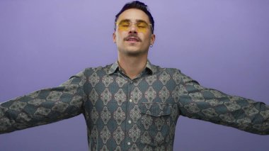 Gömleği desenli genç adam kollarını izole edilmiş mor arka plana karşı güvenli bir şekilde açıyor.