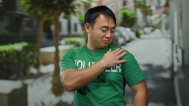 Yeşil tişörtlü genç adam şehir sokağında güvenle duruyor.