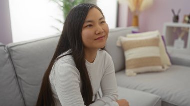 Evdeki rahat bir kanepede dinlenen bir kadın, sıcak, hoş bir oturma odasında hoş bir dekor ile çevrili, yumuşak ışıklandırma ve nötr tonlarla..