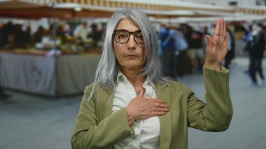 Gri saçlı bir kadın açık hava pazarında küfür jesti yapıyor. Etrafı bulanık müşterilerle çevrili. Güven ve samimiyet duygusu taşıyor..