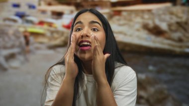 Plajda bağırarak el ele tutuşan genç Latin kökenli kadın, deniz kenarına dönüp arkadaş arıyor..