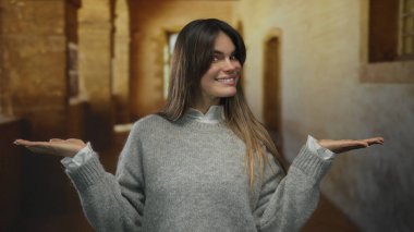 Duvarlar ve kemerlerle çevrili eski bir üniversite koridorunda elleri açık gülümseyen genç İspanyol kadın..