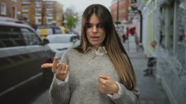 Bulanık şehir arka planı ve sonbahar ortamına sahip, konsantrasyon ve günlük tarzıyla hareketli bir caddede dikilen İspanyol kadın parmaklarını sayıyor..