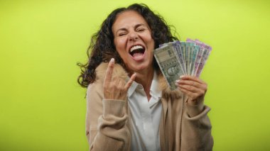 Orta yaşlı bir kadın elinde Hint rupisi notları tutarak parlak sarı bir zemin üzerinde kaya jestleri yaparak heyecan ve refahı ifade ediyor..