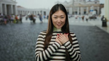 Vatikan 'da elleri göğsünde, çizgili bir bluz giymiş, geçmişi bulanık ve kaldırım taşı sokağında Aziz Peter Meydanı' nda gülümseyen bir kadın..