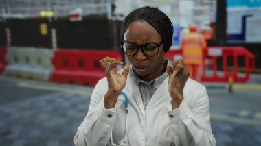 İnşaat alanındaki doktor laboratuvar önlüğü ve steteskop giyip dışarıda el sıkışık bir şekilde dikiliyor..