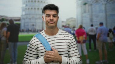 İtalya 'da sidik kulesine karşı mavi sırt çantalı genç adam çizgili tişört giyen turistlerle çevrili yazın tadını çıkarıyor..