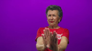 Gri saçlı, kırmızı gönüllü tişört giyen son sınıf öğrencisi kadın canlı mor arka planda duruyor..