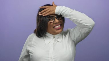 Beyaz gömlek ve gözlüklü, mor arka plan karşısında eli alnında hayal kırıklığını ifade eden bir kadın..