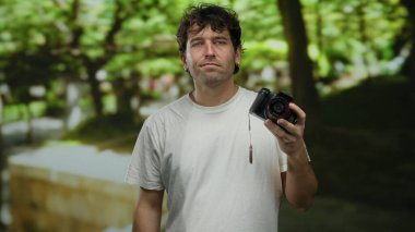Yeşil park ortamında kamerayı tutan yakışıklı bir adam güneşli bir günde doğa ve sükunete odaklanmış fotoğrafçılık anları yakalıyor.