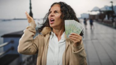 Singapur 'da, deniz kenarında orta yaşlı bir kadın, kalabalık bir liman bölgesinin yakınındaki gürültüden rahatsız olduğunu belirten bir ifadeyle, elinde Singapur doları tutuyordu..