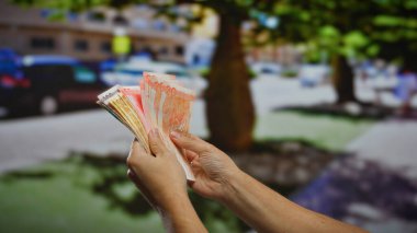 Şehir sokaklarında Filipin pesolarını sayan bir adam görünür banknotlarla kentsel yatırım kavramlarını gösteriyor ve açık hava ortamında finansal büyümeye odaklanıyor..