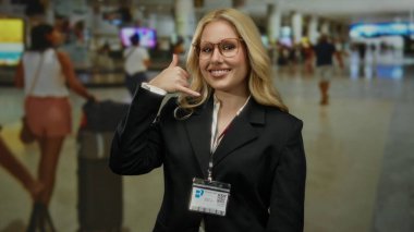 Havaalanı terminalinden bana el kol hareketi yapan genç bir kadın gülümseyen, gözlüklü, iş kıyafetli ve arka planda bulanık yolcularla beni ara..