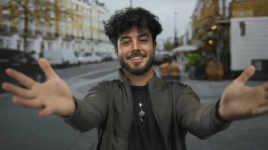Sakallı genç İspanyol bir adam şehir caddesinde kendini kucaklıyor, şehir merkezinin tadını çıkarırken kendini olumlu ifade ediyor..