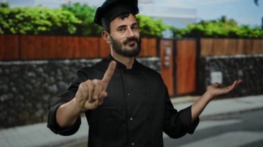 İspanyol erkek aşçı, dışarıda bir sokakta parmağını ciddi bir ifadeyle uygunsuz bir hareket yapıyor. Etrafı doğa ve kentsel unsurlarla çevrili. Eşsiz bir sahne yaratıyor..