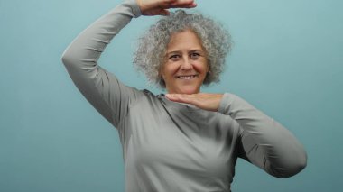 Neşeli mavi arka planda dans eden kadın enerjik ruhunu ve gri kıvırcık saçlarını sergiliyor..