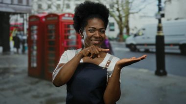 Önlüklü kadın şehir sokaklarında ikonik kırmızı telefon kulübeleriyle Palm 'ı işaret ediyor..