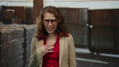 İnşaat alanında gözlük takan ve spor ceket giyen bir kadın, arka plandaki yapı malzemeleriyle farklı duygular ifade ediyor..