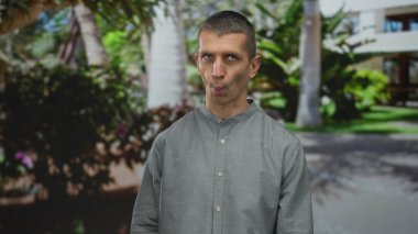 Parktaki yeşil ve modern binalarla çevrili komik suratlı adam, parlak güneş ışığı altında neşeli ve rahat bir atmosfer yaratıyor..