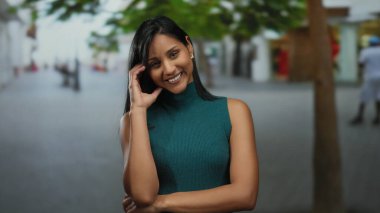 Gündüz vakti arka planda ağaçlarla sokakta gülümseyen genç bir kadın..